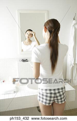 Rear view of a young woman applying face powder on her forehead in front of a mirror View Large Photo Image Stock Image - Rear view of a young woman applying face powder on her forehead in front of a mirror. Fotosearch