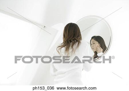 Rear view of a young woman applying face powder in front of a mirror View Large Photo Image Stock Photograph - Rear view of a young woman applying face powder in front of a mirror. Fotosearch