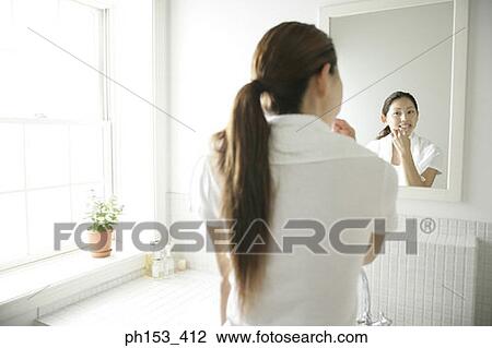 Rear view of a young woman brushing her teeth in front of a mirror View Large Photo Image Stock Image - Rear view of a young woman brushing her teeth in front of a mirror. Fotosearch
