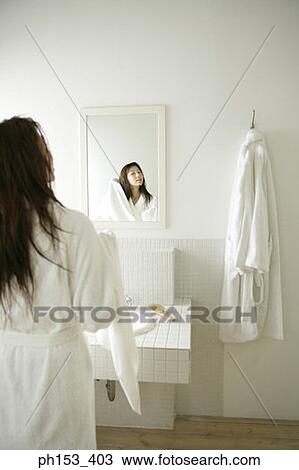 Stock Image - Rear view of a young woman drying her hair with a towel in front of a mirror. Fotosearch