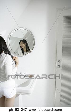 Rear view of a young woman holding her hair in front of a mirror View Large Photo Image Stock Photo - Rear view of a young woman holding her hair in front of a mirror. Fotosearch
