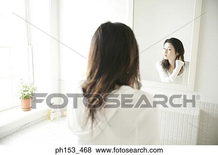 Stock Photo - Rear view of a young woman looking in a mirror. Fotosearch