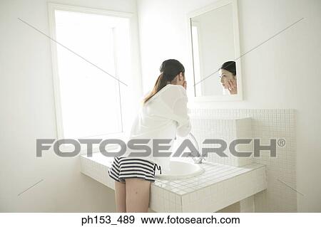 Rear view of a young woman looking in a mirror and torching her face View Large Photo Image Stock Photo - Rear view of a young woman looking in a mirror and torching her face. Fotosearch