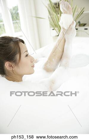 Stock Photo - Rear view of a young woman scrubbing her leg with a sponge in a bathtub. Fotosearch