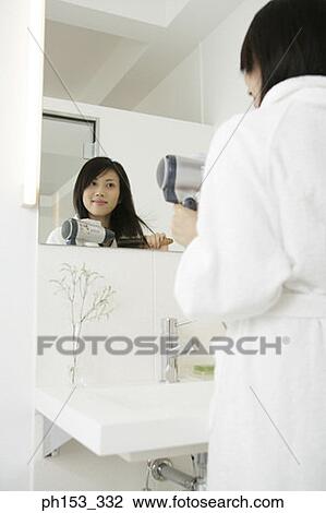 Rear view of a young woman standing in front of a mirror and drying her hair with a hair dryer View Large Photo Image Stock Image - Rear view of a young woman standing in front of a mirror and drying her hair with a hair dryer. Fotosearch
