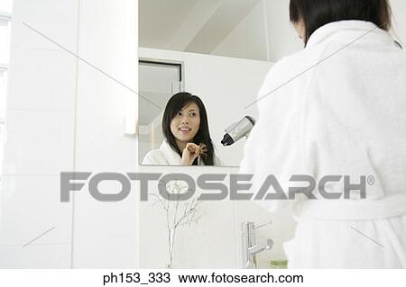 Rear view of a young woman standing in front of a mirror and drying her hair with a hair dryer View Large Photo Image Stock Image - Rear view of a young woman standing in front of a mirror and drying her hair with a hair dryer. Fotosearch