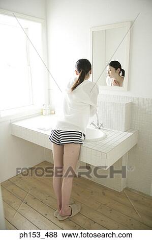 Rear view of a young woman standing in front of a mirror View Large Photo Image Stock Photo - Rear view of a young woman standing in front of a mirror. Fotosearch