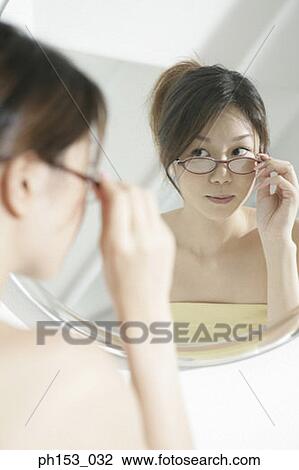 Reflection of a young woman adjusting her eyeglasses in a mirror View Large Photo Image Stock Image - Reflection of a young woman adjusting her eyeglasses in a mirror . Fotosearch