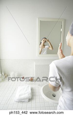 Stock Image - Reflection of a young woman applying soap on her forehead in a mirror . Fotosearch