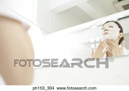 Reflection of a young woman in the mirror applying a facial mask View Large Photo Image Picture - Reflection of a young woman in the mirror applying a facial mask. Fotosearch