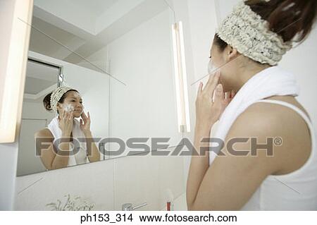 Picture - Side profile of a young woman applying soap on her face. Fotosearch