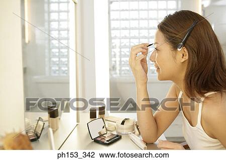 Side profile of a young woman applying make-up in front of a dressing table View Large Photo Image Stock Image - Side profile of a young woman applying make-up in front of a dressing table. Fotosearch