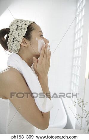Stock Photo - Side profile of a young woman applying soap on her face. Fotosearch