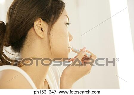 Stock Photo - Side profile of a young woman applying lipstick. Fotosearch