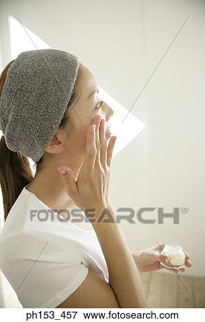 Side profile of a young woman applying moisturizer on her face View Large Photo Image Stock Photo - Side profile of a young woman applying moisturizer on her face. Fotosearch