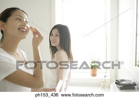 Side profile of a young woman applying face powder on her face with another young woman looking at her View Large Photo Image Stock Photograph - Side profile of a young woman applying face powder on her face with another young woman looking at her. Fotosearch