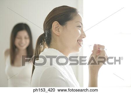 Side profile of a young woman brushing her teeth with another young woman standing in the background View Large Photo Image Stock Image - Side profile of a young woman brushing her teeth with another young woman standing in the background. Fotosearch