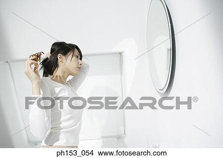 Side profile of a young woman holding a hair clip and looking into a mirror View Large Photo Image Picture - Side profile of a young woman holding a hair clip and looking into a mirror. Fotosearch