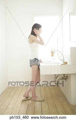 Stock Image - Side profile of a young woman looking at a mirror. Fotosearch