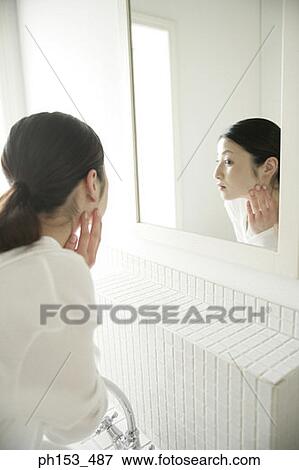 Side profile of a young woman looking into a mirror and touching her face View Large Photo Image Stock Photo - Side profile of a young woman looking into a mirror and touching her face. Fotosearch