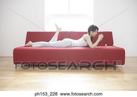 Side profile of a young woman lying on a couch and applying nail polish on her fingernails View Large Photo Image Stock Photo - Side profile of a young woman lying on a couch and applying nail polish on her fingernails. Fotosearch