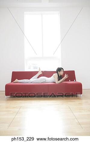 Side profile of a young woman lying on a couch and applying nail polish on her fingernails View Large Photo Image Stock Photo - Side profile of a young woman lying on a couch and applying nail polish on her fingernails. Fotosearch