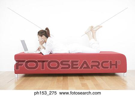Side profile of a young woman lying on a couch and using a laptop View Large Photo Image Stock Photography - Side profile of a young woman lying on a couch and using a laptop. Fotosearch