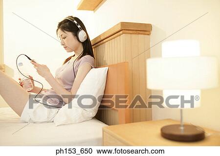 Side profile of a young woman reclining on the bed and listening to music View Large Photo Image Stock Image - Side profile of a young woman reclining on the bed and listening to music. Fotosearch