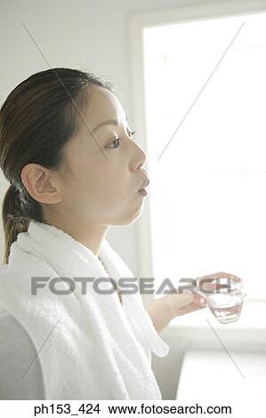 Side profile of a young woman rinsing her mouth and holding a glass of water View Large Photo Image Picture - Side profile of a young woman rinsing her mouth and holding a glass of water. Fotosearch