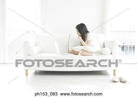 Side profile of a young woman sitting on a couch and using a laptop View Large Photo Image Stock Image - Side profile of a young woman sitting on a couch and using a laptop. Fotosearch