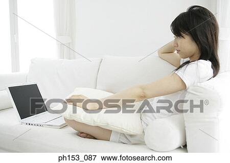Side profile of a young woman sitting on a couch and using a laptop View Large Photo Image Stock Photo - Side profile of a young woman sitting on a couch and using a laptop. Fotosearch