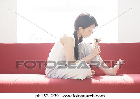 Side profile of a young woman sitting on a couch and applying nail polish View Large Photo Image Stock Photo - Side profile of a young woman sitting on a couch and applying nail polish. Fotosearch