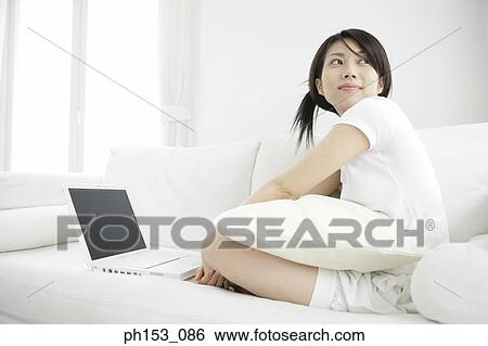 Side profile of a young woman sitting on a couch and using a laptop View Large Photo Image Stock Photograph - Side profile of a young woman sitting on a couch and using a laptop. Fotosearch
