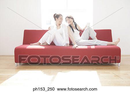 Two young women sitting on a couch and holding cups of coffee View Large Photo Image Stock Image - Two young women sitting on a couch and holding cups of coffee. Fotosearch