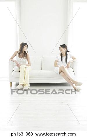 Two young women sitting on a couch and looking at each other View Large Photo Image Stock Photo - Two young women sitting on a couch and looking at each other. Fotosearch