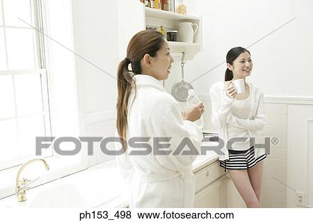 Two young women standing and smiling in the kitchen View Large Photo Image Stock Photo - Two young women standing and smiling in the kitchen. Fotosearch