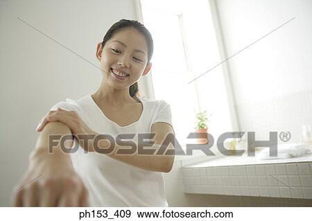 Stock Photo - Young woman applying moisturizer on her hand in the bathroom. Fotosearch