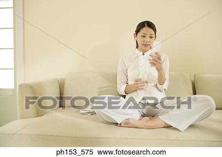 Young woman listening to music on a couch and using a mobile phone View Large Photo Image Stock Photography - Young woman listening to music on a couch and using a mobile phone. Fotosearch
