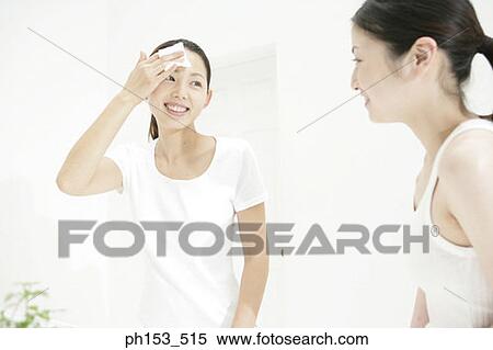 Young woman looking at another young woman wiping her face with a cotton pad View Large Photo Image Stock Photography - Young woman looking at another young woman wiping her face with a cotton pad. Fotosearch