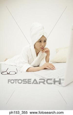 Young woman lying on the bed and using a laptop View Large Photo Image Stock Photography - Young woman lying on the bed and using a laptop. Fotosearch