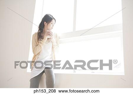 Young woman relaxing on a window sill and holding a mug View Large Photo Image Stock Photo - Young woman relaxing on a window sill and holding a mug. Fotosearch