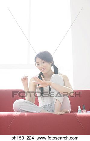 Young woman sitting on a couch and filing her fingernails View Large Photo Image Picture - Young woman sitting on a couch and filing her fingernails. Fotosearch