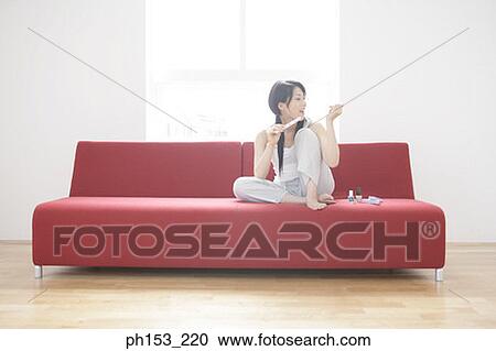 Young woman sitting on a couch and filing her fingernails View Large Photo Image Stock Image - Young woman sitting on a couch and filing her fingernails. Fotosearch