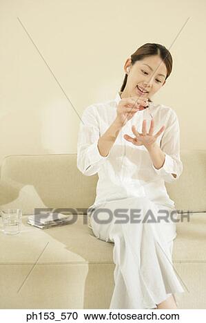 Young woman sitting on a couch and applying nail polish View Large Photo Image Stock Image - Young woman sitting on a couch and applying nail polish. Fotosearch