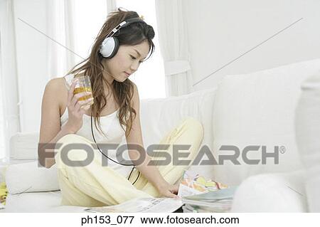 Young woman sitting on a couch and listening to music View Large Photo Image Stock Photo - Young woman sitting on a couch and listening to music. Fotosearch