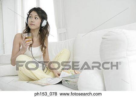 Young woman sitting on a couch and listening to music View Large Photo Image Stock Photo - Young woman sitting on a couch and listening to music. Fotosearch