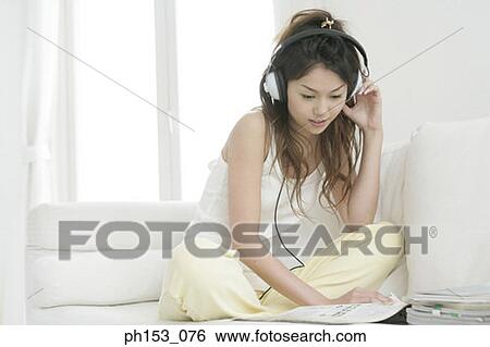 Young woman sitting on a couch and listening to music View Large Photo Image Stock Photograph - Young woman sitting on a couch and listening to music. Fotosearch
