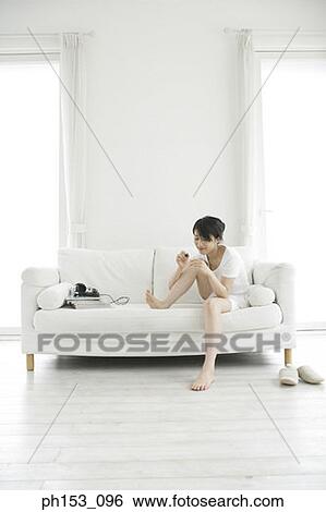 Young woman sitting on a couch and applying nail polish View Large Photo Image Stock Photograph - Young woman sitting on a couch and applying nail polish. Fotosearch