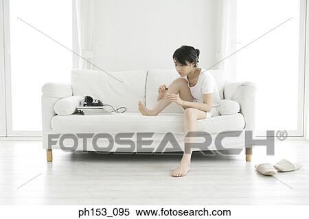Stock Photography - Young woman sitting on a couch and applying nail polish. Fotosearch