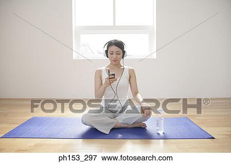 Young woman sitting on an exercise mat and listening to music View Large Photo Image Stock Photo - Young woman sitting on an exercise mat and listening to music. Fotosearch